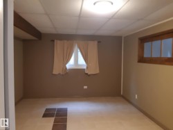 Spacious master bedroom featuring neutral wall tones, square tile flooring with a decorative inlay, a dropped ceiling with recessed lighting, and a window with wood trim - 