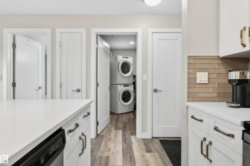 Kitchen area featuring white cabinetry, light-toned wood-finish flooring, and a stacked washer and dryer unit - 209 1029 173 Stnw, Edmonton, AB - Indoor