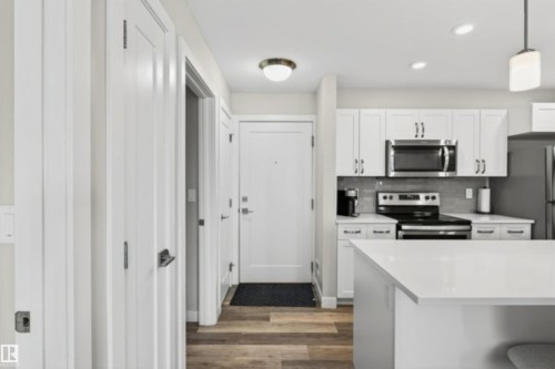 Contemporary kitchen featuring white cabinetry, stainless steel appliances, a white island, and wood-finish flooring - 209 1029 173 Stnw, Edmonton, AB - Indoor Photo Showing Kitchen