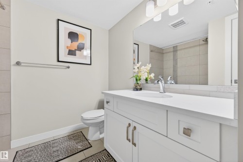 Bathroom featuring a white vanity with an integrated sink, polished chrome faucet, and expansive wall mirror - 209 1029 173 Stnw, Edmonton, AB - Indoor Photo Showing Bathroom