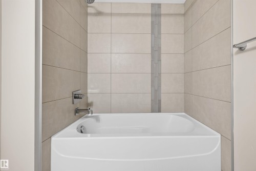 White bathtub with chrome fixtures, surrounded by light-toned wall tiles - 209 1029 173 Stnw, Edmonton, AB - Indoor Photo Showing Bathroom