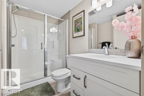 Bathroom featuring a glass-enclosed shower with integrated seating, white vanity with a single basin, single-handle chrome faucet, rectangular mirror, and a three-light vanity fixture - 209 1029 173 Stnw, Edmonton, AB - Indoor Photo Showing Bathroom