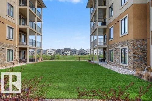 Spacious green lawn bordered by two multi-story buildings featuring stucco and stone veneer exteriors - 209 1029 173 Stnw, Edmonton, AB - Outdoor With Balcony