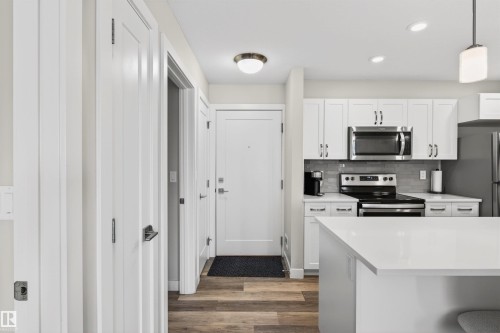 Modern kitchen featuring white shaker cabinetry, stainless steel appliances, a subway tile backsplash, and a large island with a solid surface countertop - 209 1029 173 Stnw, Edmonton, AB - Indoor Photo Showing Kitchen