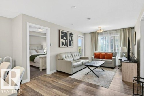 Open-concept living space featuring wood-finish flooring, a contemporary ceiling light fixture, and a balcony door with natural light - 209 1029 173 Stnw, Edmonton, AB - Indoor Photo Showing Living Room