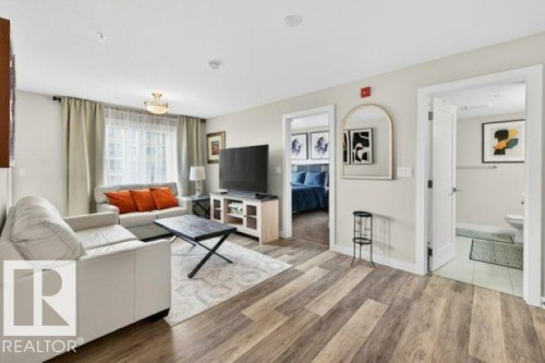 Open-concept living space featuring wood-finish flooring, a contemporary ceiling light fixture, and a large window with privacy sheers - 209 1029 173 Stnw, Edmonton, AB - Indoor Photo Showing Living Room