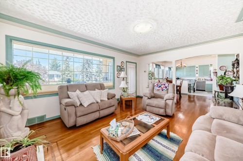 Bright living area featuring a wide picture window with grid detailing, polished wood-finish flooring, and a decorative ceiling - 11309 115 Street, Edmonton, AB - Indoor Photo Showing Living Room