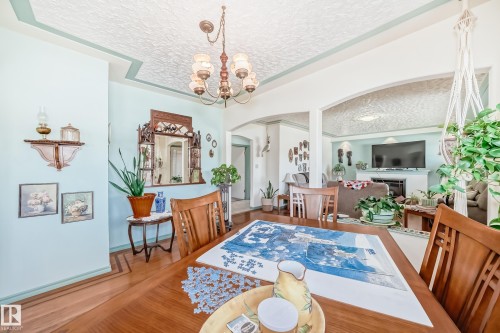 Formal dining area featuring wood-finish flooring with inlay details, a decorative ceiling with a central chandelier, and arched doorways opening to an additional living space with a fireplace - 11309 115 Street, Edmonton, AB - Indoor Photo Showing Dining Room