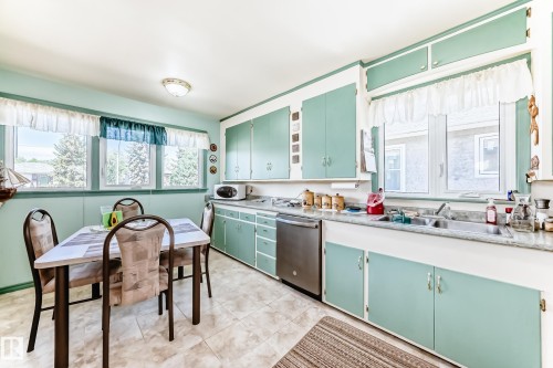 Eat-in kitchen featuring ample cabinetry, dual basin stainless steel sink, stainless steel dishwasher, and tiled flooring - 11309 115 Street, Edmonton, AB - Indoor