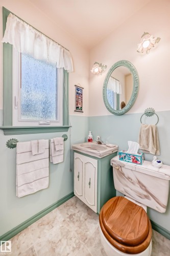 Bathroom featuring a single window with privacy glass, a vanity with cabinet storage, an oval mirror, two wall-mounted light fixtures, and tile flooring - 11309 115 Street, Edmonton, AB - Indoor Photo Showing Bathroom