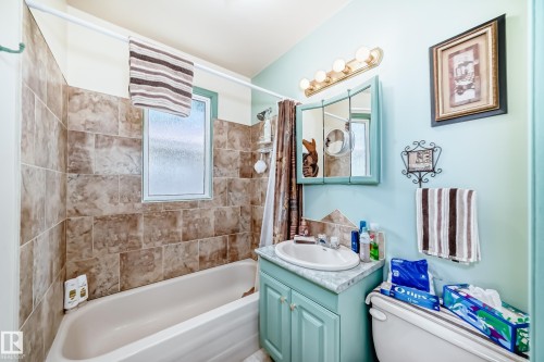 Bathroom featuring a white bathtub, ceramic wall tiling, a privacy window, a vanity with an integrated sink, and a mirrored medicine cabinet - 11309 115 Street, Edmonton, AB - Indoor Photo Showing Bathroom