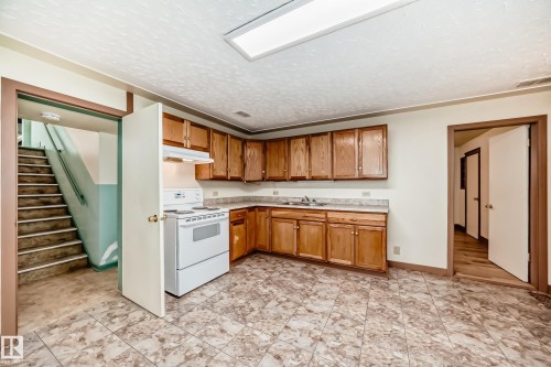 Functional kitchen featuring wood-finish cabinetry, light-toned countertops, and a white electric range with an overhead hood - 11309 115 Street, Edmonton, AB - Indoor Photo Showing Kitchen With Double Sink
