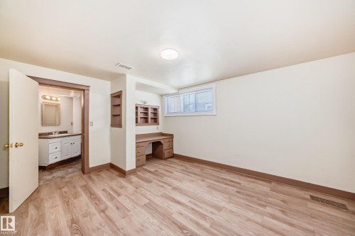 Versatile room featuring wood-finish flooring, a built-in desk with shelving, and a window - 11309 115 Street, Edmonton, AB - Indoor