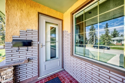 Covered entryway featuring a storm door with a full-length glass panel, stucco wall texture, and stacked brick veneer siding - 11309 115 Street, Edmonton, AB - Outdoor With Deck Patio Veranda With Exterior