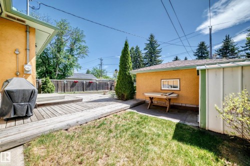 Expansive backyard featuring a wood-finish deck, a concrete patio area, a detached garage with an exterior window, and mature perimeter trees - 11309 115 Street, Edmonton, AB - Outdoor With Deck Patio Veranda With Exterior
