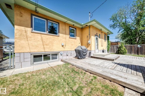 Exterior stucco siding with a concrete block foundation, featuring a private wooden deck and a mature treeline - 11309 115 Street, Edmonton, AB - Outdoor With Exterior