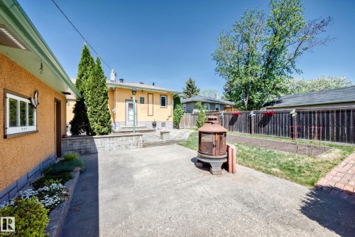 Concrete patio with a stone retaining wall, mature perimeter trees, and a privacy fence - 11309 115 Street, Edmonton, AB - Outdoor