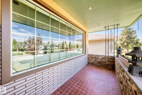 Covered front porch featuring a large grid-pattern window, red diamond-patterned floor tiles, a stacked stone pony wall, and decorative wrought iron railing - 11309 115 Street, Edmonton, AB - Outdoor With Deck Patio Veranda With Exterior