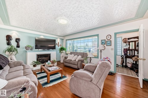 Hardwood flooring complements a white fireplace with an integrated firebox - 11309 115 Street, Edmonton, AB - Indoor Photo Showing Living Room With Fireplace