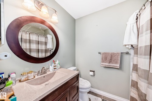 Bathroom featuring a dark wood-finish vanity with an integrated sink and light-toned countertop, a round framed mirror, and a three-light vanity fixture - 9110 180A Avenue, Edmonton, AB - Indoor Photo Showing Bathroom