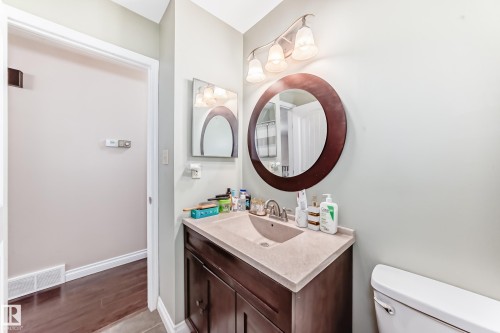 Bathroom featuring a wood-finish vanity with an integrated sink, a circular framed mirror, and a three-light fixture - 9110 180A Avenue, Edmonton, AB - Indoor Photo Showing Bathroom