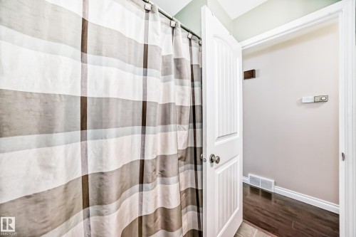 Bathroom featuring a shower area with a striped curtain, a paneled door with brushed nickel hardware, and wood-finish flooring - 9110 180A Avenue, Edmonton, AB - Indoor Photo Showing Bathroom