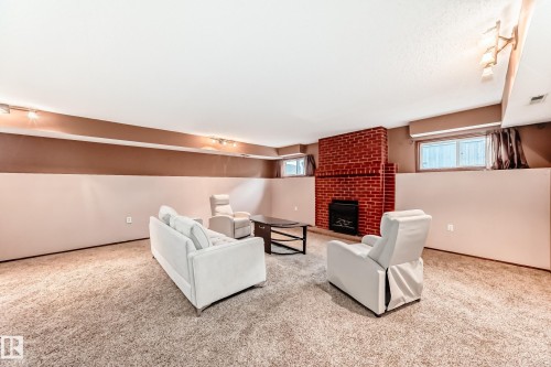 Spacious lower-level room featuring a brick-clad fireplace, track lighting, neutral carpeting, and multiple windows - 9110 180A Avenue, Edmonton, AB - Indoor With Fireplace