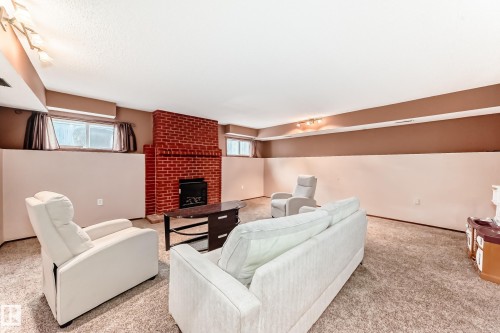 Spacious room featuring a brick fireplace with a black insert, carpeted flooring, and recessed windows - 9110 180A Avenue, Edmonton, AB - Indoor With Fireplace
