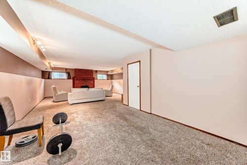 Spacious lower-level room featuring a brick fireplace, track lighting, carpeted flooring, and a white interior door with dark trim - 9110 180A Avenue, Edmonton, AB - Indoor Photo Showing Other Room