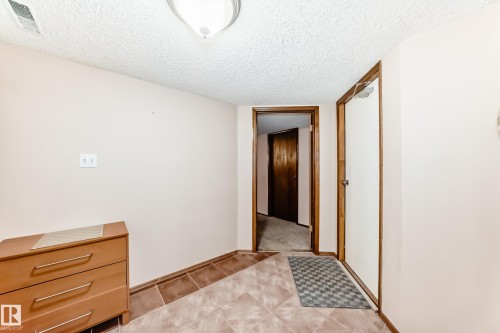 Hallway featuring ceramic tile flooring, a textured ceiling, and wood-trim doorways - 9110 180A Avenue, Edmonton, AB - Indoor Photo Showing Other Room