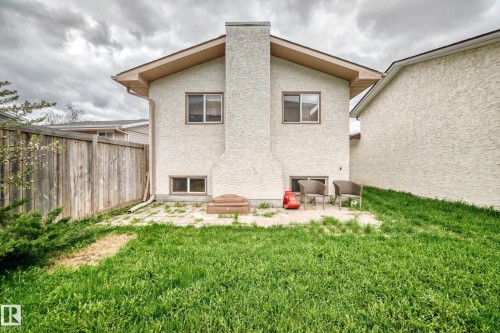Rear stucco exterior featuring a prominent chimney, upper and lower windows, and a ground-level patio area - 9110 180A Avenue, Edmonton, AB - Outdoor With Exterior