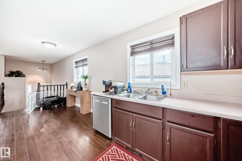 Kitchen area featuring a double basin stainless steel sink, dark wood-finish cabinetry, a light-toned countertop, and an integrated dishwasher - 9110 180A Avenue, Edmonton, AB - Indoor Photo Showing Kitchen With Double Sink