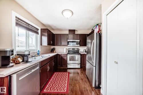 Kitchen featuring rich wood-finish flooring, dark wood cabinetry, white countertops, and stainless steel appliances including a refrigerator, range, microwave, and dishwasher - 9110 180A Avenue, Edmonton, AB - Indoor Photo Showing Kitchen With Double Sink