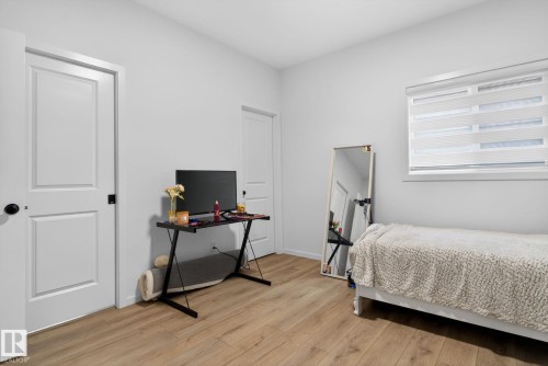Light-filled room featuring wood-finish flooring, white paneled doors with black hardware, and a window with horizontal blinds - 7011 177 Avenue, Edmonton, AB - Indoor Photo Showing Bedroom
