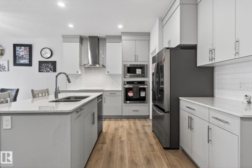 Modern kitchen featuring a central island with an undermount sink, light-toned countertops, and wood-finish flooring - 7011 177 Avenue, Edmonton, AB - Indoor Photo Showing Kitchen With Double Sink With Upgraded Kitchen