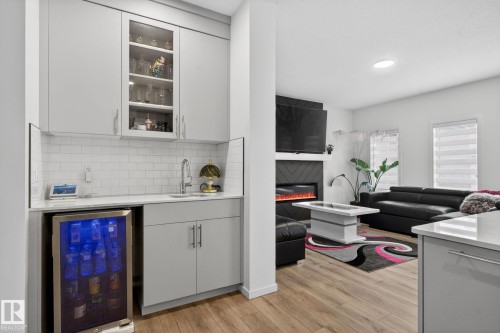 Integrated wet bar featuring a built-in beverage cooler, undermount sink, and light gray cabinetry with glass-front uppers - 7011 177 Avenue, Edmonton, AB - Indoor