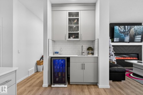 Compact wet bar featuring light gray cabinetry, glass-front upper cabinets, subway tile backsplash, and a built-in beverage refrigerator - 7011 177 Avenue, Edmonton, AB - Indoor