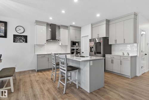 Contemporary kitchen featuring a central island, stainless steel appliances, white subway tile backsplash, light wood-finish flooring, and recessed lighting - 7011 177 Avenue, Edmonton, AB - Indoor Photo Showing Kitchen With Upgraded Kitchen