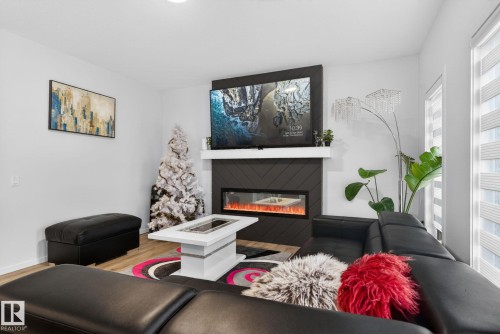 Living area featuring a chevron-patterned fireplace surround with an integrated electric fireplace, a white mantel, and wood-finish flooring - 7011 177 Avenue, Edmonton, AB - Indoor Photo Showing Living Room With Fireplace