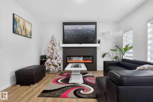 Living area featuring a floor-to-ceiling accent wall with a fireplace, a white mantel, and wood-finish flooring - 7011 177 Avenue, Edmonton, AB - Indoor Photo Showing Living Room With Fireplace