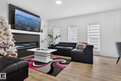 Living area featuring light wood-finish flooring and a contemporary fireplace with a linear insert and dark chevron-patterned surround - 7011 177 Avenue, Edmonton, AB - Indoor Photo Showing Living Room With Fireplace