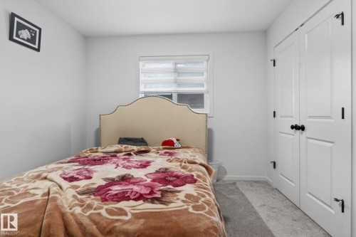 Bedroom featuring light gray walls, a window with horizontal blinds, and a built-in closet with white bifold doors and matte black hardware - 7011 177 Avenue, Edmonton, AB - Indoor Photo Showing Bedroom