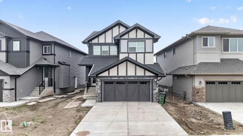 Modern Tudor-style home featuring a prominent two-car garage, stone accents, decorative timber framing, a paved driveway, and a covered entry - 7011 177 Avenue, Edmonton, AB - Outdoor With Facade