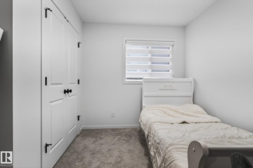 Interior room featuring neutral wall paint, gray carpeting, a window with horizontal blinds, and white bi-fold doors with black hardware - 7011 177 Avenue, Edmonton, AB - Indoor Photo Showing Bedroom