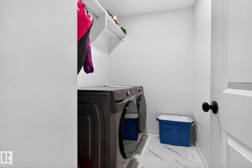 Dedicated laundry area featuring a modern front-load washer and dryer set, white wall shelving, and white baseboards - 7011 177 Avenue, Edmonton, AB - Indoor Photo Showing Laundry Room