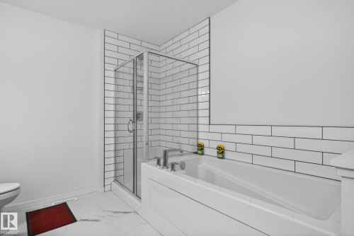 Full bathroom featuring a walk-in shower with clear glass enclosure, a white soaking tub with integrated paneling, and subway tile accents on walls - 7011 177 Avenue, Edmonton, AB - Indoor Photo Showing Bathroom