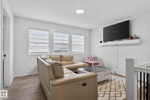 Bright room with three large windows, wood-finish flooring, recessed ceiling light, and a wall-mounted floating shelf - 7011 177 Avenue, Edmonton, AB - Indoor Photo Showing Living Room
