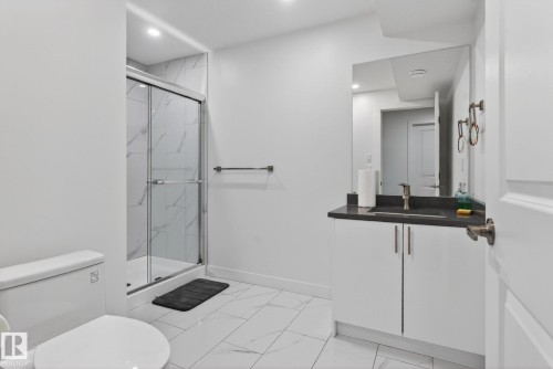 Contemporary bathroom with a glass-enclosed shower featuring large format tile, a modern vanity with a dark countertop, white cabinetry with brushed metal pulls, and recessed lighting - 7011 177 Avenue, Edmonton, AB - Indoor Photo Showing Bathroom