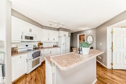 Kitchen featuring white cabinetry, wood-finish flooring, a breakfast bar with a laminate countertop, white appliances, and track lighting - 