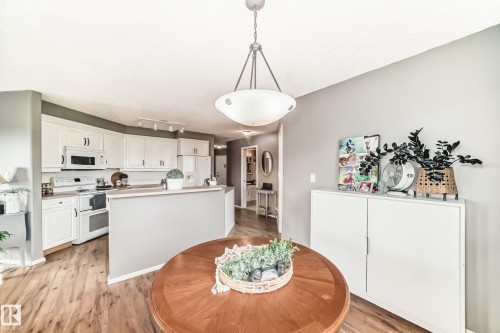 Open-concept kitchen and dining area featuring white cabinetry, light countertops, wood-finish flooring, and a contemporary pendant light fixture - 331 9704 174 Street, Edmonton, AB - Indoor